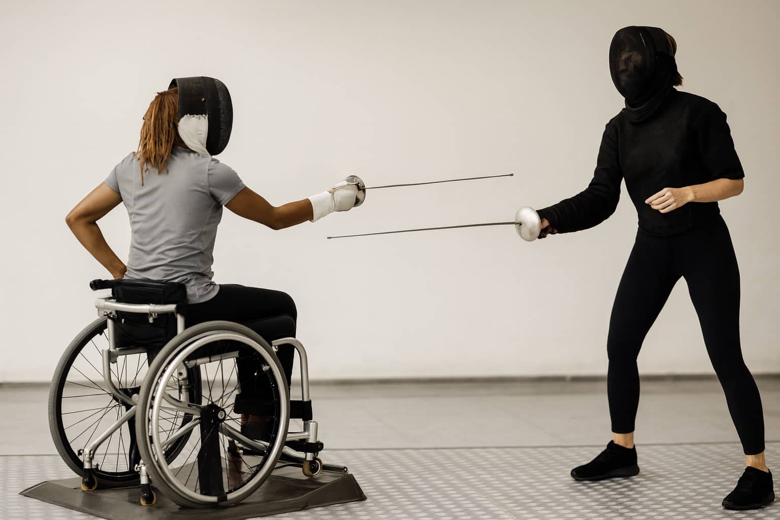  Duel d’escrime entre une sportive en fauteuil roulant et une adversaire valide, discipline handisport reconnue.
